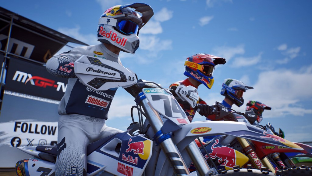 Tre motociclisti di motocross in abbigliamento da gara, schierati su moto da cross, pronti per la competizione. Sullo sfondo si vede un logo Red Bull e un cielo sereno.